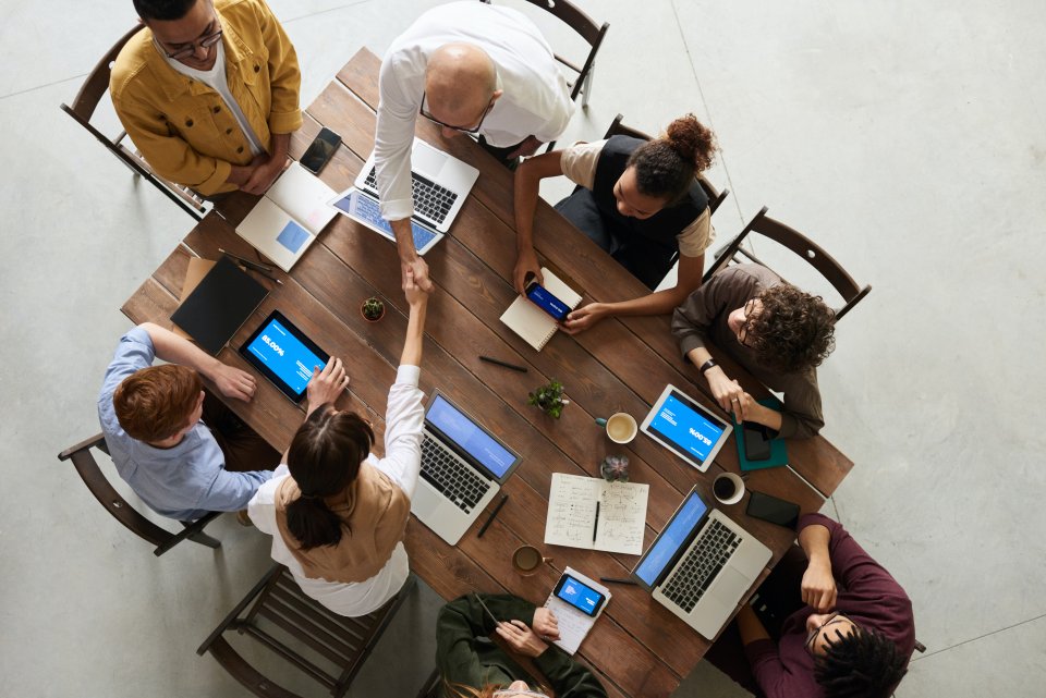 Over the top view of a table surrounded by people with laptops/tablets, collaborating